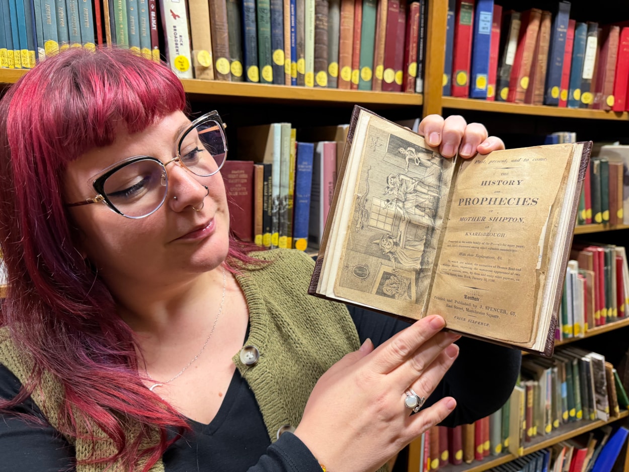 Mother Shipton book: Librarian Sally Hughes with a vivid woodcut illustration that depicts a famous scene when the soothsayer Mother Shipton was reputedly confronted by nobles sent to her cottage by the powerful Cardinal Wolsey, who was furious she had made the treasonous prediction that he would never set foot inside the city of York.
Under threat of being burned at the stake, a defiant Mother Shipton was said to have plucked a handkerchief from her head and thrown it into the fire, proclaiming that if it did not burn, then neither would she.