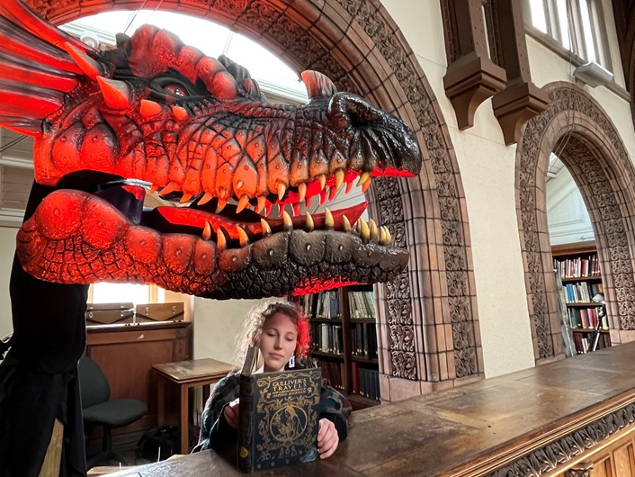 Fantasy at Leeds Central Library: Library and  Digital Assistant Heather Edwards reads a vintage copy of Gulliver's Travels, illustrated by Arthur Rachkam while a dragon created artist Anne Stokes looks on.