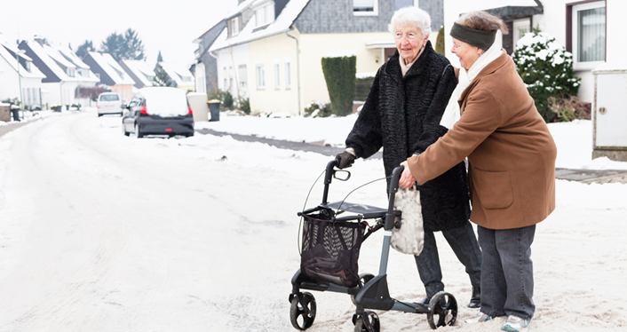 A woman helping an elderly woman cross a snowy street