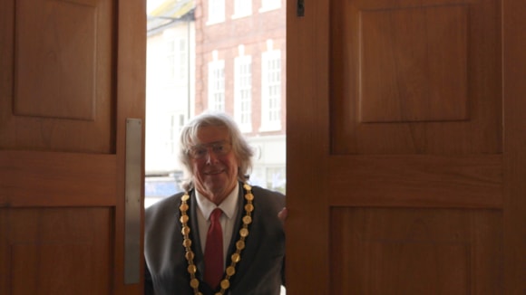 View of Councillor Graham Deasy Mayor of Exmouth opening the doors of the town hall, from the inside, with shops in the background