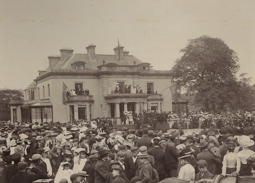 A sepia toned image of a grand looking Grant Lodge with lots of people in Victorian dress milling around outside it.