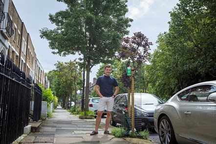 A person in shorts, pictured on the street beside a sponsored tree.