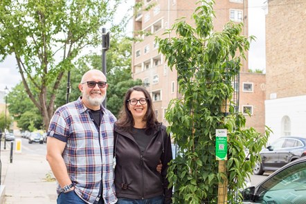 Two people, pictured on the street beside a sponsored tree in an empty tree pit outside their house.
