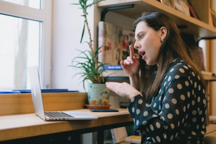 A young female sits in front of a laptop in a library - she is signing to the screen.