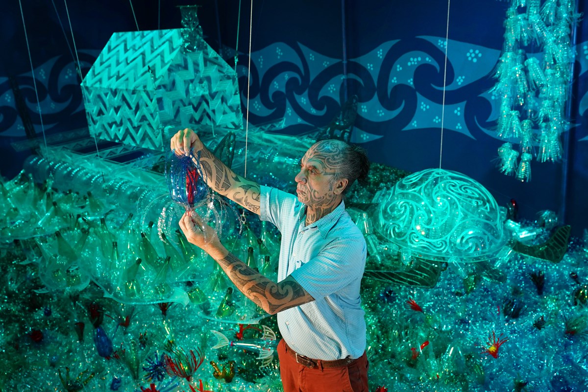 Artist George Nuku puts the finishing touches to the installation of the artwork Bottled Ocean 2123, an imagined underwater landscape made from recycled plastic. The work will go on show in the exhibition Rising Tide: Art and Environment in Oceania, which opens on August 12 at the National Museum of Scotland. Image credit: Stewart Attwood