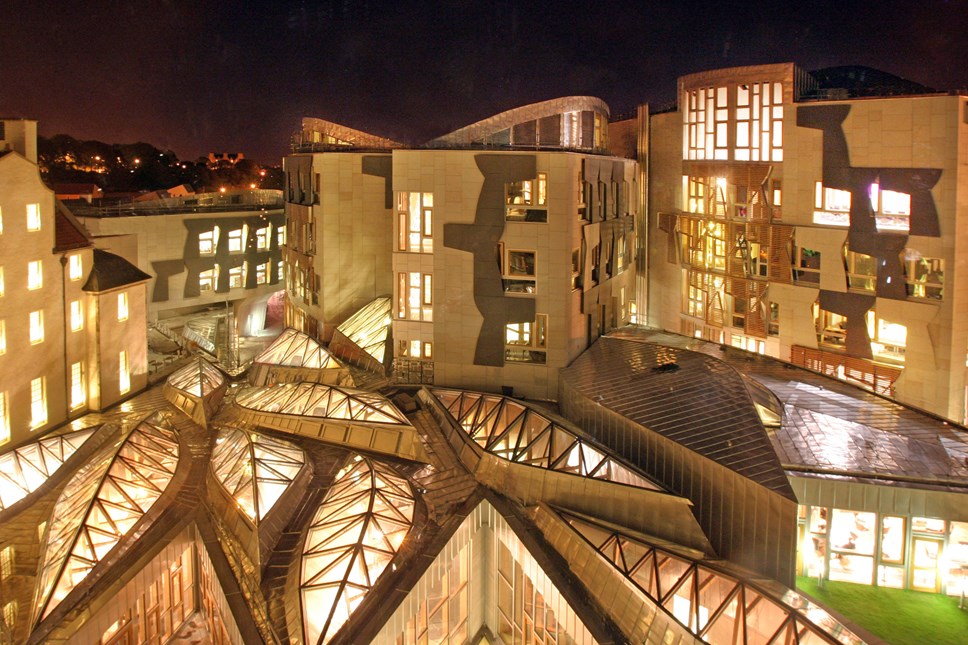 Image of the Scottish Parliament building lit up in the evening.