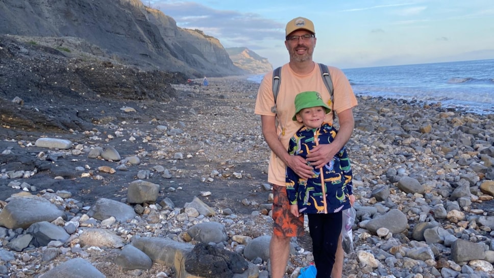 Man and boy stand on pebbled beach.