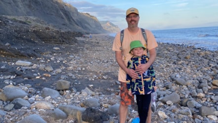 Man and boy stand on pebbled beach.