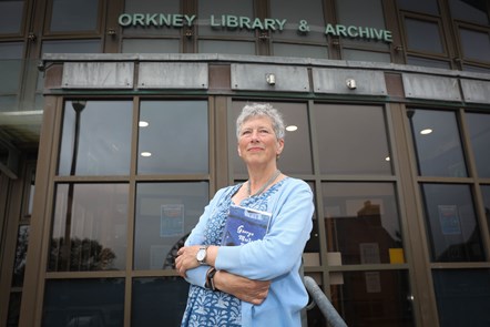 2021–22 Scots Scriever, Alison Miller outside Orkney Library and Archive. She is pictured standing and holding a book in her arms.