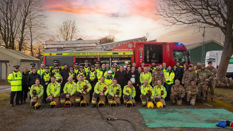 large group of emergency service and army personnel in high-vis uniforms stood in front of a fire engine