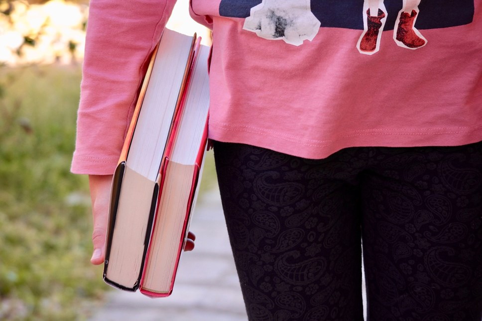 Child in pink top carrying two books, close up of hand and books