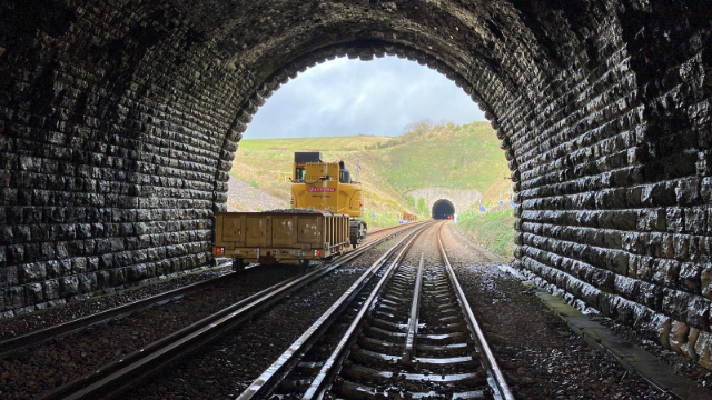 An RRV digger with a ballast clearing attachment towing a wagon full of new ballast at Bincombe Tunnel near Upwey