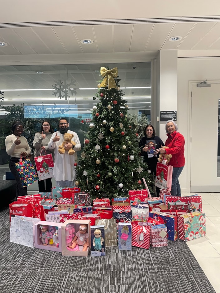 CFL Christmas Gifting 1: Pictured shows bags of gifts in front of a Christmas tree First Direct office in Leeds, with representatives holding gift bag.