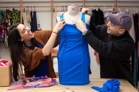 Two Fashion Enter employees work on a blue dress together
