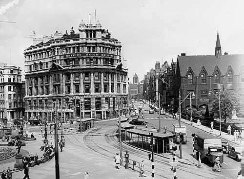 City Square Credit Leeds Civic Trust: City Square: Undated City Square and view up Park Row taken from Queen's Hotel. From left, flower beds and statues of City Square. Behind which is the end of Infirmary Street. The Norwich Union building is on the corner of Park Row and at the end of Park Row St Anne's Cathedral is visible. At the front on the right is Priestley Hall and the archway to the grounds of Mill Hill Chapel. Tram stops and period cars are visible in the foreground. Credit Leeds Civic Trust.