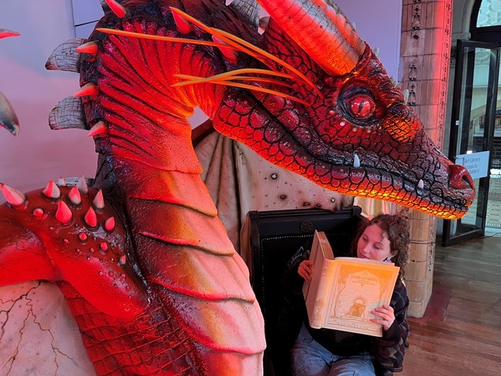 Fantasy at Leeds Central Library: Library and  Digital Assistant Heather Edwards reads a vintage copy of the fairytales of Hans Christian Anderson , illustrated by Kay Nielsen, while a dragon created artist Anne Stokes looks on.