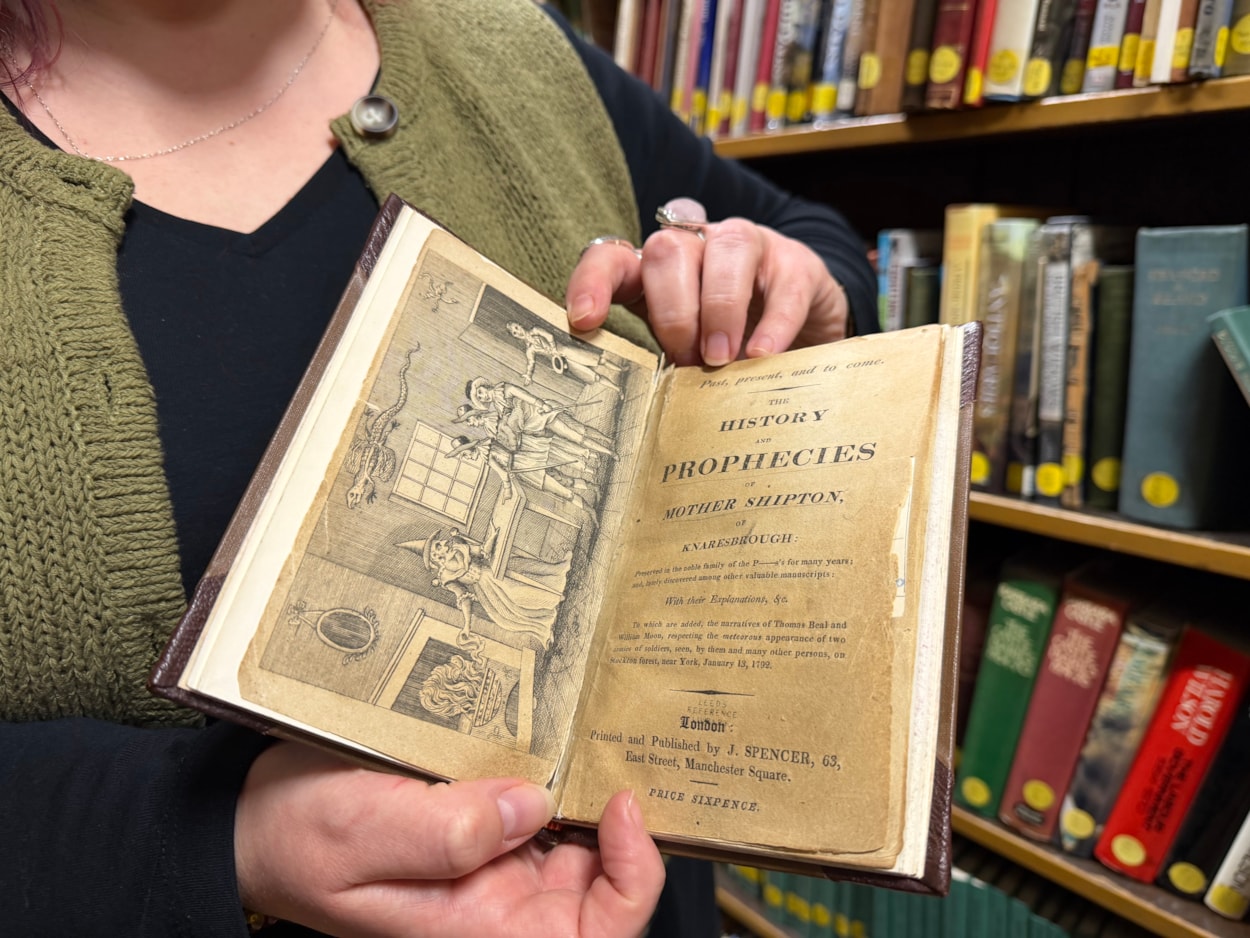 Mother Shipton book: Librarian Sally Hughes with a vivid woodcut illustration that depicts a famous scene when the soothsayer Mother Shipton was reputedly confronted by nobles sent to her cottage by the powerful Cardinal Wolsey, who was furious she had made the treasonous prediction that he would never set foot inside the city of York.
Under threat of being burned at the stake, a defiant Mother Shipton was said to have plucked a handkerchief from her head and thrown it into the fire, proclaiming that if it did not burn, then neither would she.