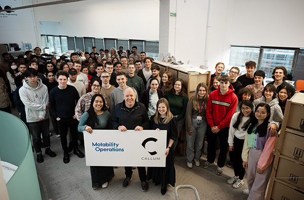 Two students win a placement: Three people stand at front of room filled with students holding sign with Motability and Callum logos.