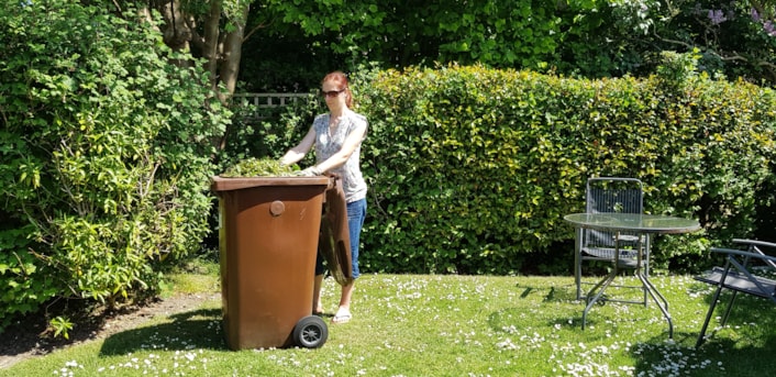 Brown bin garden waste: Image of a garden with a lady filling her brown bin with garden waste