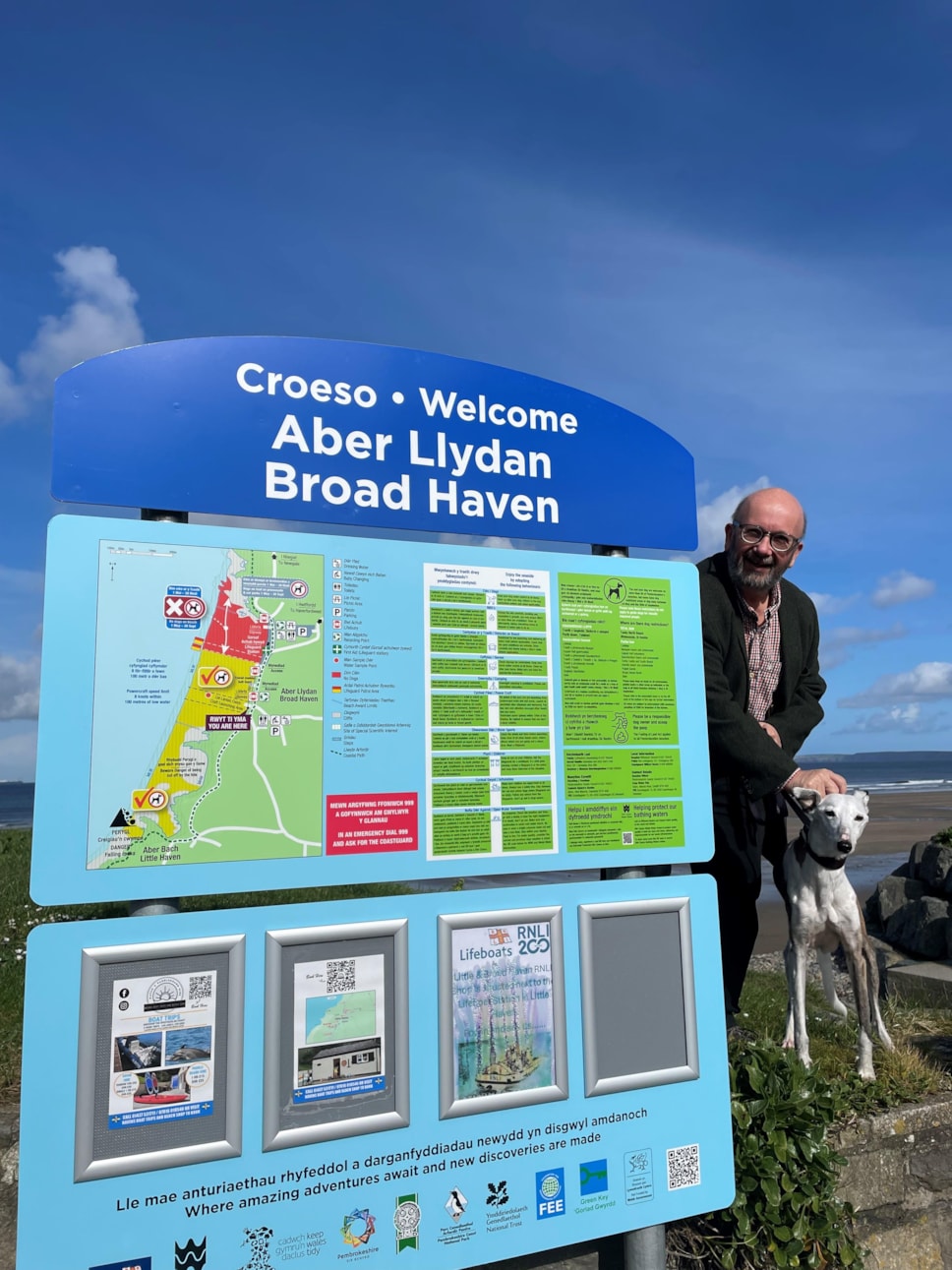 Y Cynghorydd Rhys Sinnett wrth ymyl un o'r arwyddion cyfyngiadau cŵn newydd yn Aberllydan