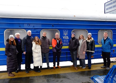 Steve Montgomery, First Rail, Andy Bagnall, Rail Partners, David Brown, Arriva and others stand in front of a shelled Ukrainian Railways train