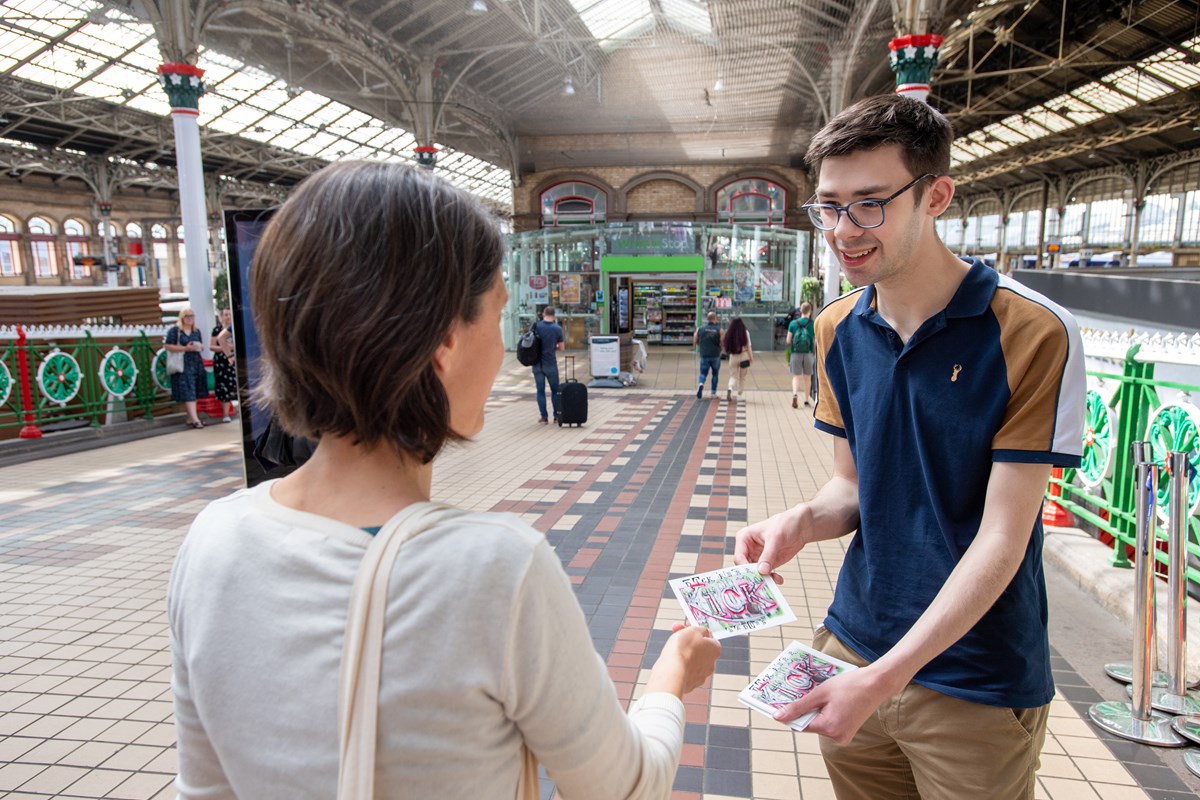 Harry, intern from DFN Project SEARCH, hands out postcards at Preston station to raise awareness of the Dick, Kerr Ladies football team