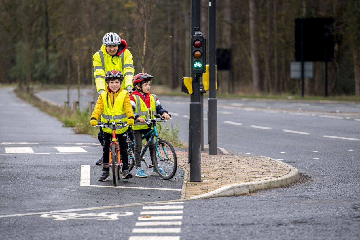 East Leeds Orbital Route cycling family: Two small children and their father using a cycling crossing at Moortown Roundabout, Leeds