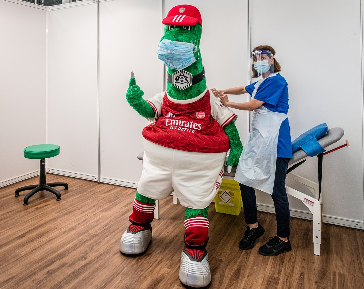 Arsenal mascot Gunnersaurus (left) gets a Covid-19 jab from a frontline member of staff at an Islington vaccination centre
