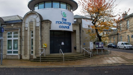 The image shows the front of the Moray Council headquarters building, featuring the council's name in blue letters on a light colored wall.