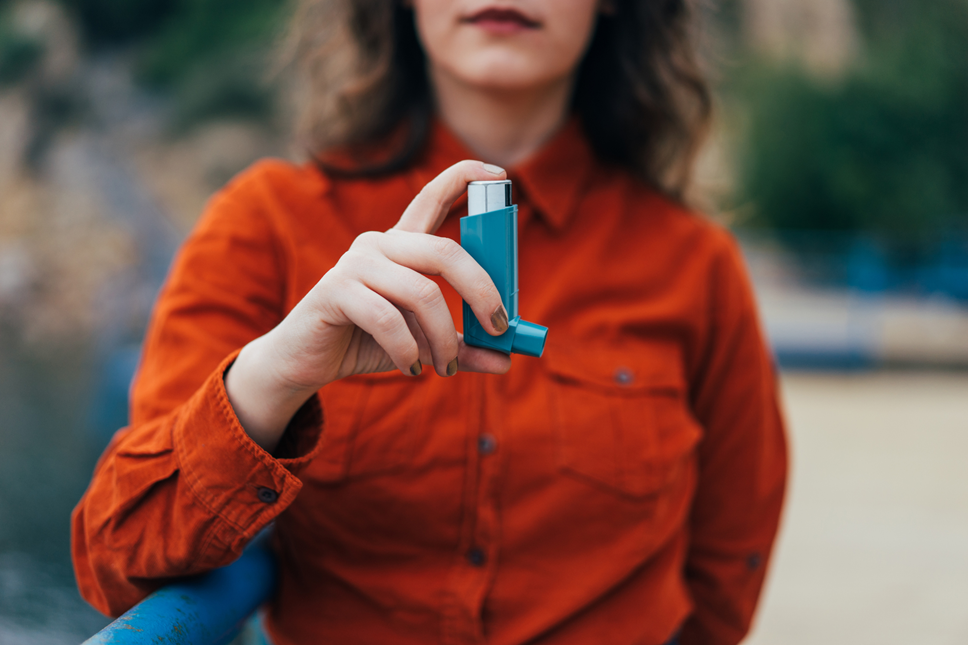 Person standing outside and holding a blue inhaler