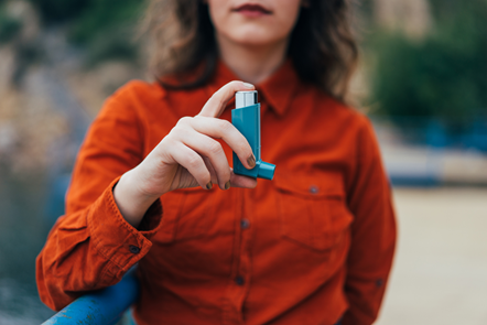 Person standing outside and holding a blue inhaler
