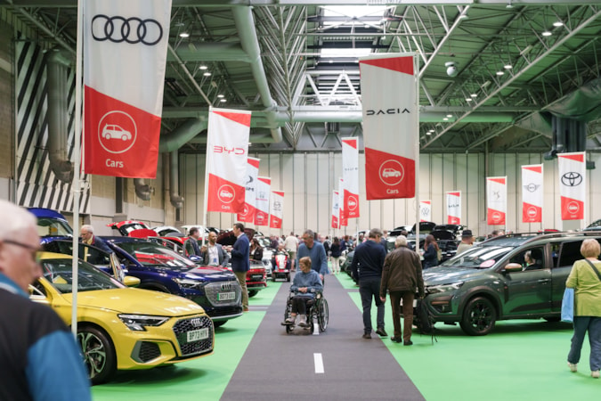 Big Event Birmingham showroom: Wide-angle view of Birmingham Big Event showroom. Man pushes woman in wheelchair towards camera looking at cars on display