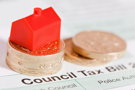 Wee red monopoly house sits on a stack of three pound coins, which sit on top of a paper council tax bill.