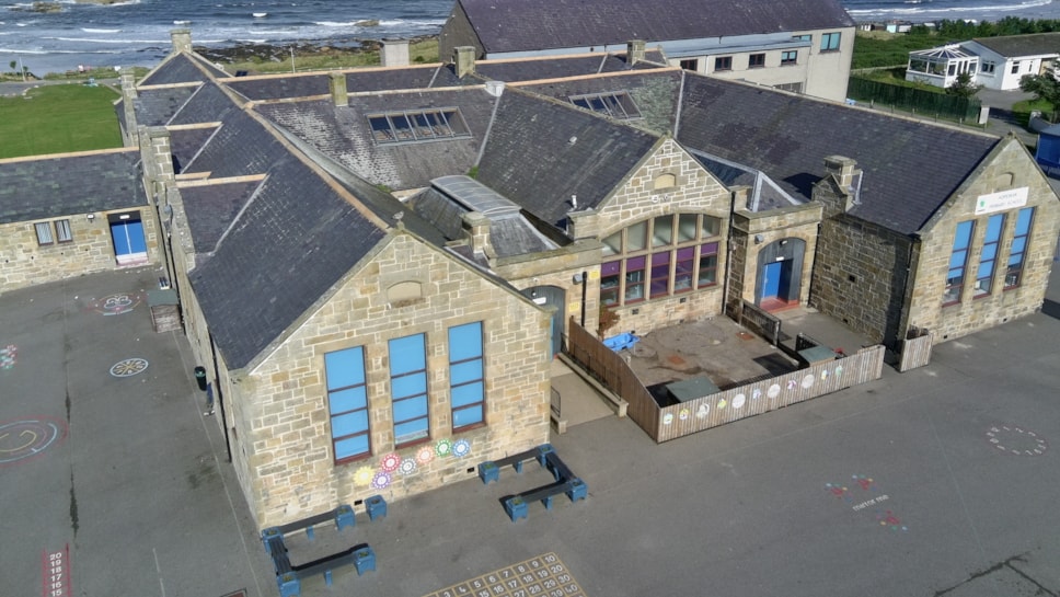 Overhead view of Hopeman Primary School, a stone building with blue-framed windows and a gabled roof.