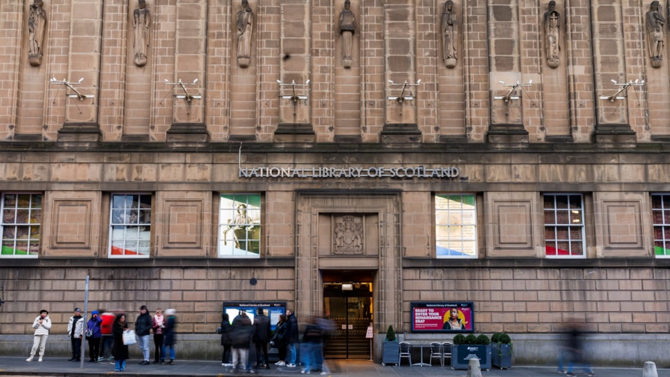 The facade of the George IV Bridge building, Edinburgh. People on the street look at information signs next to the main door.