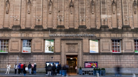 The facade of the George IV Bridge building, Edinburgh. People on the street look at information signs next to the main door.