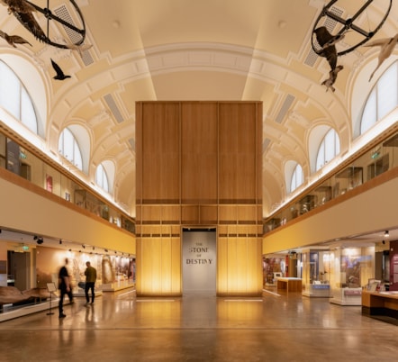 A photo of the inside of Perth Museum which shows a large, airy room with a high, rounded ceiling and displays around the outside of the room. There is a large wooden box in the middle which says 'The Stone of Destiny'