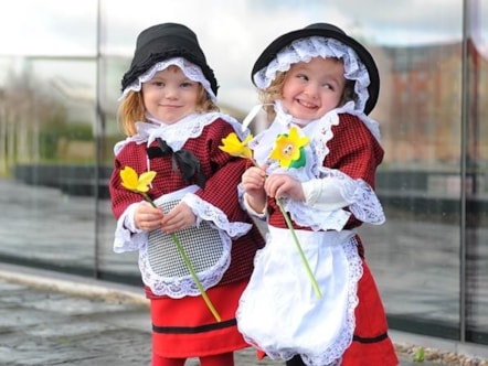 Two girls in Welsh costumes holding daffodils celebrating St. David's Day