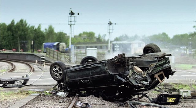 THREE MOTORISTS A WEEK DICING WITH DEATH AT LEVEL CROSSINGS: Image of upturned car from tv advert