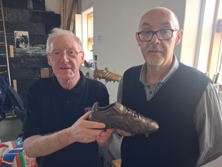 Two men holding a bronze effect football boot replica