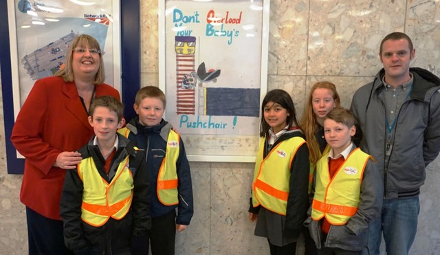 Pupils' safety posters at Leeds: (L-R): Helen Dawson, Leeds station manager; Sam Goldie; Luke Lazenby; Siriwan Maguire; Lizzie Woodward; Dylan Teague and Richard Cracknell from Leeds City Council with Luke's design on the concourse of Leeds station.