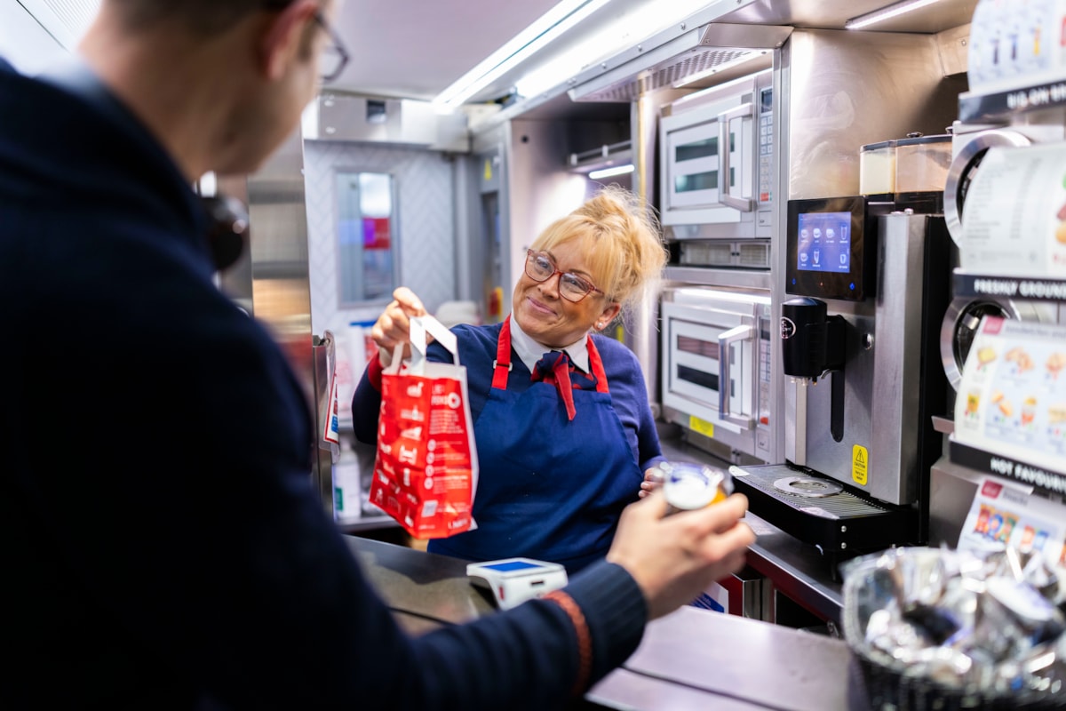 A CUSTOMER PICKING UP THEIR HOT DRINK AND FREE MUFFIN FROM THE ON BOARD CAFE BAR