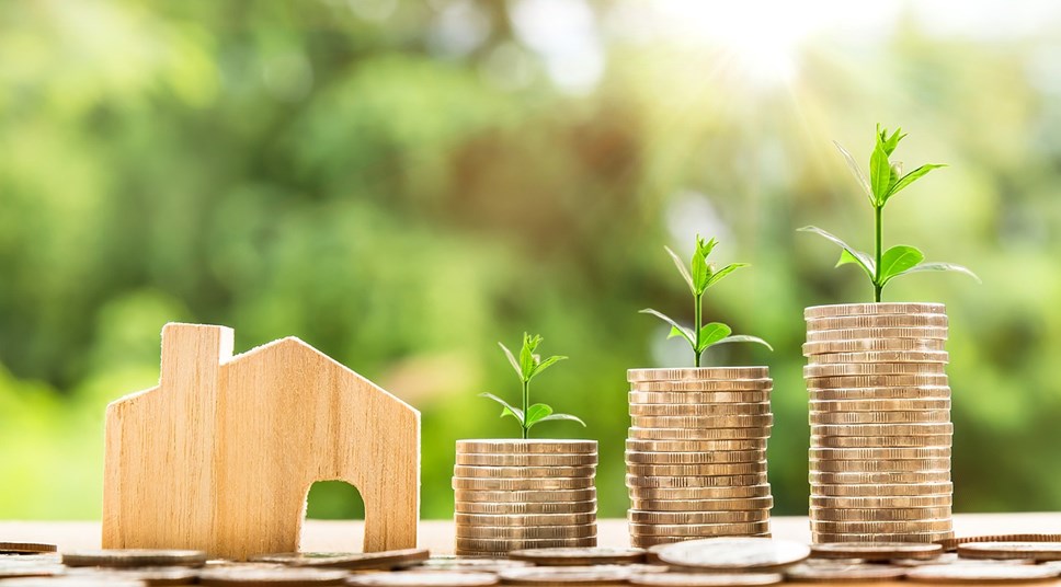 stacks of coins with green sprouts next to wooden house shape