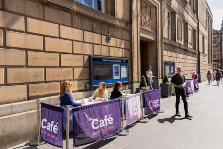 Street level shot of the National Library of Scotland on George IV Bridge. People sit at the tables outside. Others exit the building.