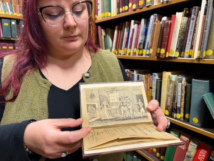 Mother Shipton book: Librarian Sally Hughes with a vivid woodcut illustration that depicts a famous scene when the soothsayer Mother Shipton was reputedly confronted by nobles sent to her cottage by the powerful Cardinal Wolsey, who was furious she had made the treasonous prediction that he would never set foot inside the city of York.
Under threat of being burned at the stake, a defiant Mother Shipton was said to have plucked a handkerchief from her head and thrown it into the fire, proclaiming that if it did not burn, then neither would she.