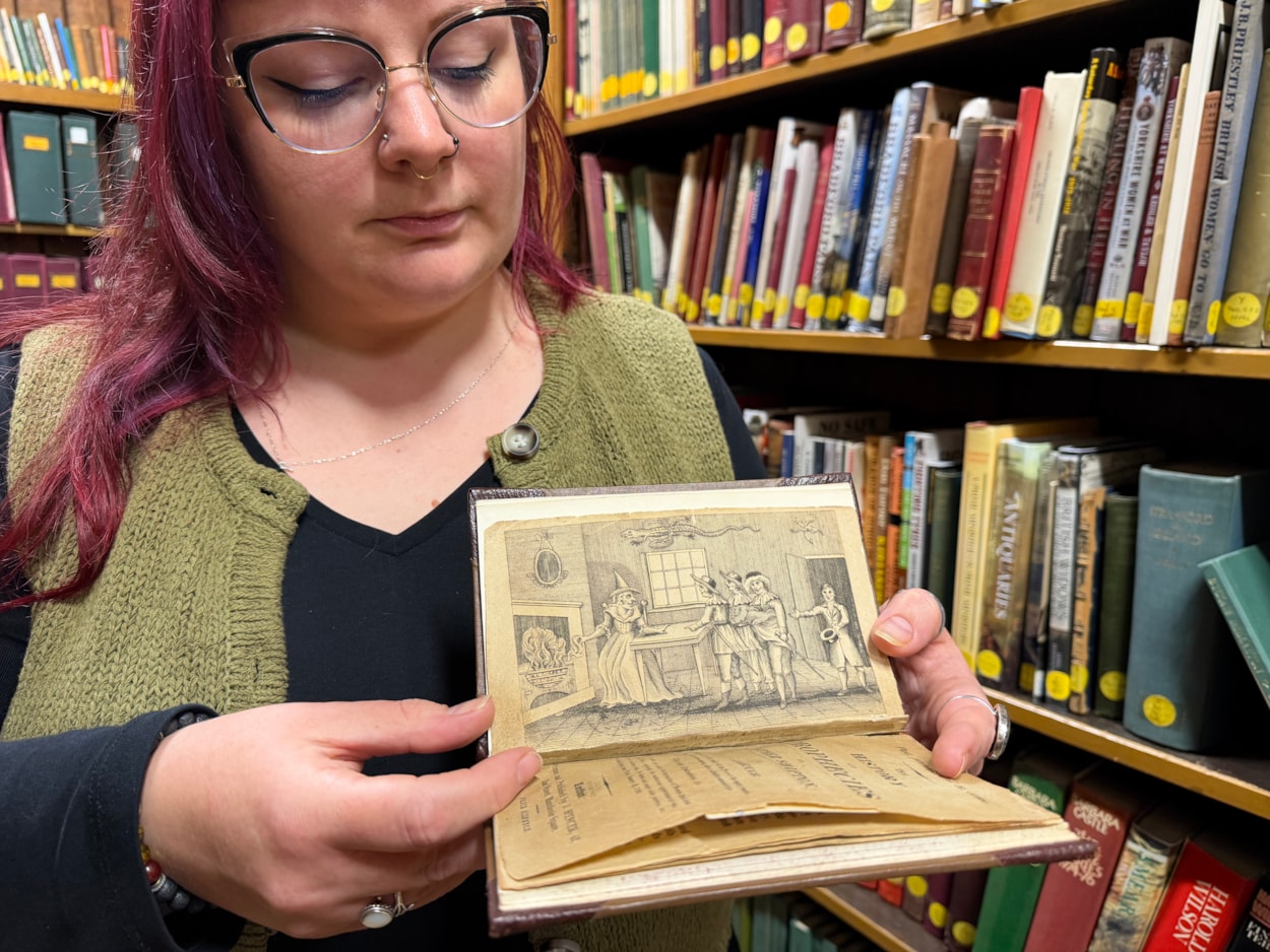 Mother Shipton book: Librarian Sally Hughes with a vivid woodcut illustration that depicts a famous scene when the soothsayer Mother Shipton was reputedly confronted by nobles sent to her cottage by the powerful Cardinal Wolsey, who was furious she had made the treasonous prediction that he would never set foot inside the city of York.
Under threat of being burned at the stake, a defiant Mother Shipton was said to have plucked a handkerchief from her head and thrown it into the fire, proclaiming that if it did not burn, then neither would she.