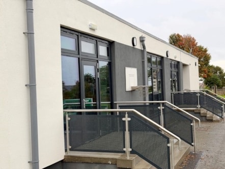 Refurbished school exterior with white walls, dark-framed doors and windows, steps and metal handrails.