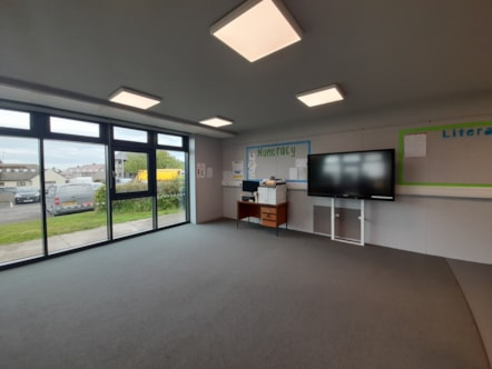 Spacious school learning area with large windows, grey flooring and an interactive display screen.