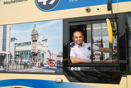 A bus driver leans out of the window of a bus in Brighton