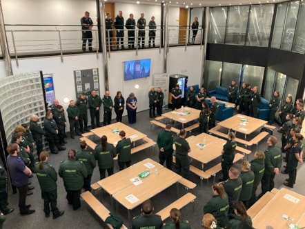 A two-storey room with several tables and lots of ambulance employees stood still with heads lowered.